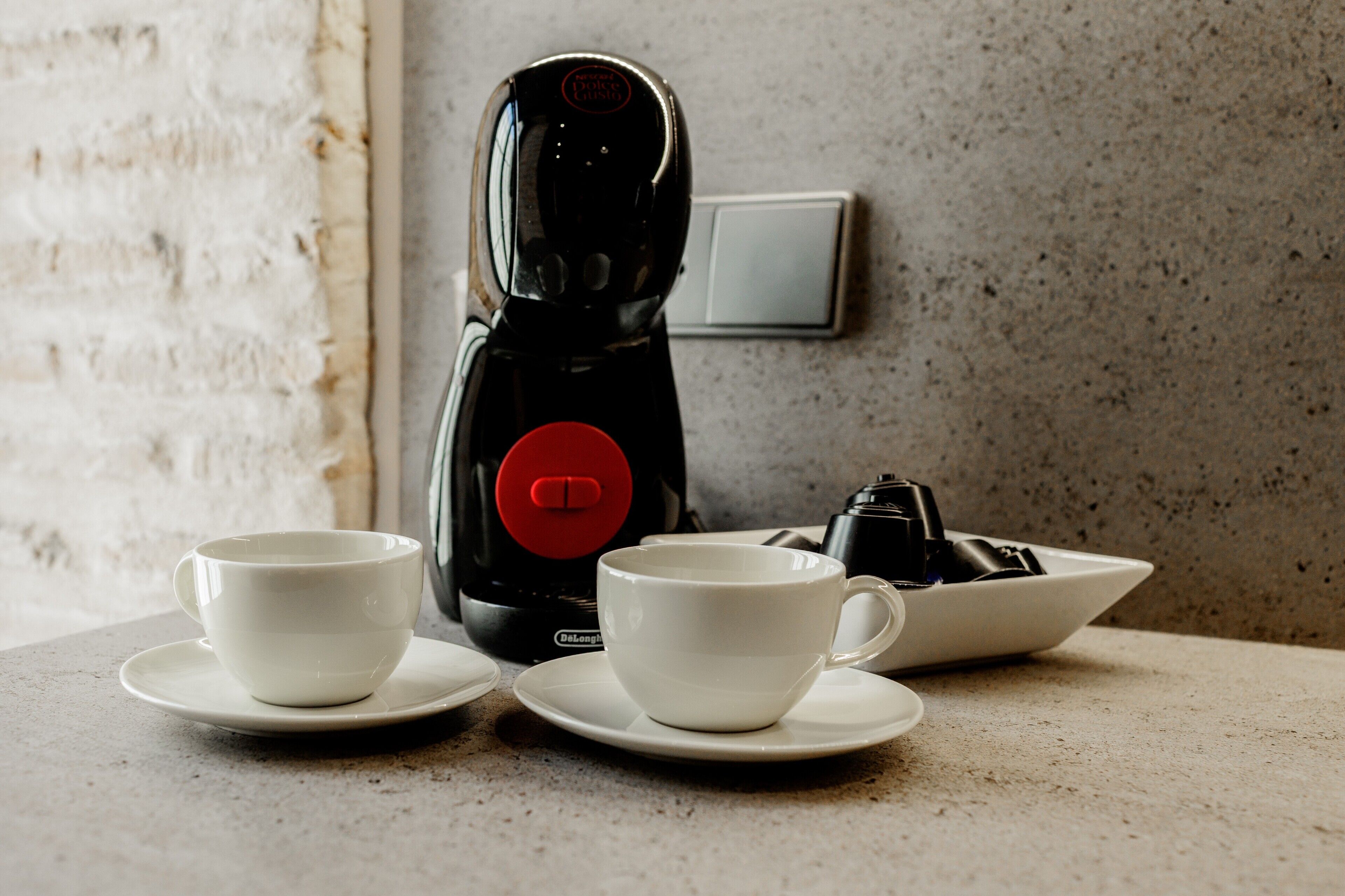 Une machine à café, deux tasses blanches et une assiette sur un plan de travail.