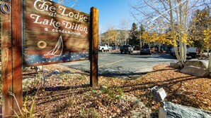 A wooden sign for The Lodge at Lake Dillon, a condominium, with a parking lot and autumn trees in the background. - Condo Near Dillon Marina - Near 3 Ski Resorts Plus Dining & Shops (Dillon)