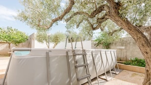 Une grande piscine blanche, dotée d’un escalier, entourée d’arbres et bordée d’un mur en béton.