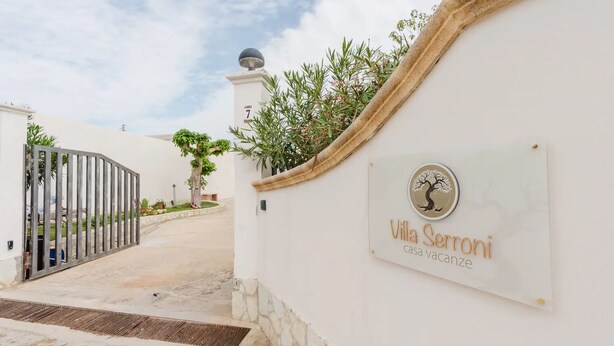 Une entrée fermée par un portail mène à la villa Sermoni, une maison proposée en location de vacances, avec un chemin dégagé qui conduit au portail.