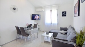 A modern living room with a grey sofa, a dining table with chairs, a flat-screen TV, and a decorative wall clock. - Quiet holiday apartment with balcony (Umag)