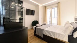 A modern hotel room with a bed, a flat-screen TV mounted on the wall, a small seating area, and a window with curtains. - Spacious 2-bedroom flat in the centre of Madrid. (Madrid)