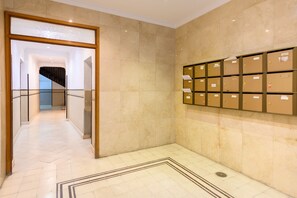 Um corredor com piso de mármore, guarda-corpo de vidro e uma parede com caixas organizadoras.