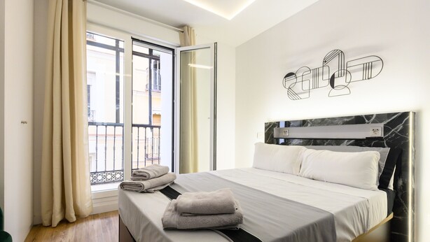A hotel room with a bed, a window with curtains, a balcony, and a wall-mounted artwork. - Spacious 2-bedroom flat in the centre of Madrid. (Madrid)