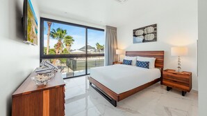 Una camera d'albergo con un letto grande, una scrivania, una sedia, una televisione e un balcone con vista sulle palme.
