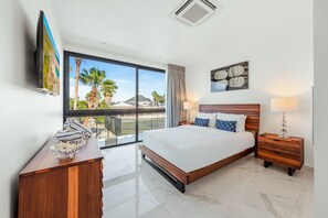 A hotel room with a large bed, a desk, a chair, a TV, and a balcony with a view of palm trees. - Romantic 1BR Getaway w/ Private Jacuzzi by Bocobay (Noord)