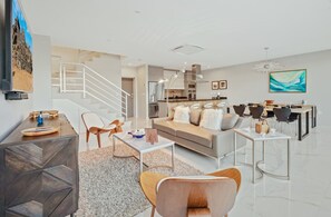 A modern living room with a sofa, coffee table, and chairs, a kitchen with a dining area, and a staircase. - Romantic 1BR Getaway w/ Private Jacuzzi by Bocobay (Noord)