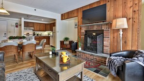 A modern living room with a glass coffee table, a fireplace, and a dining area with wooden furniture. - Mountain Green Condo 2b4 2 Bedroom Condo (Killington)