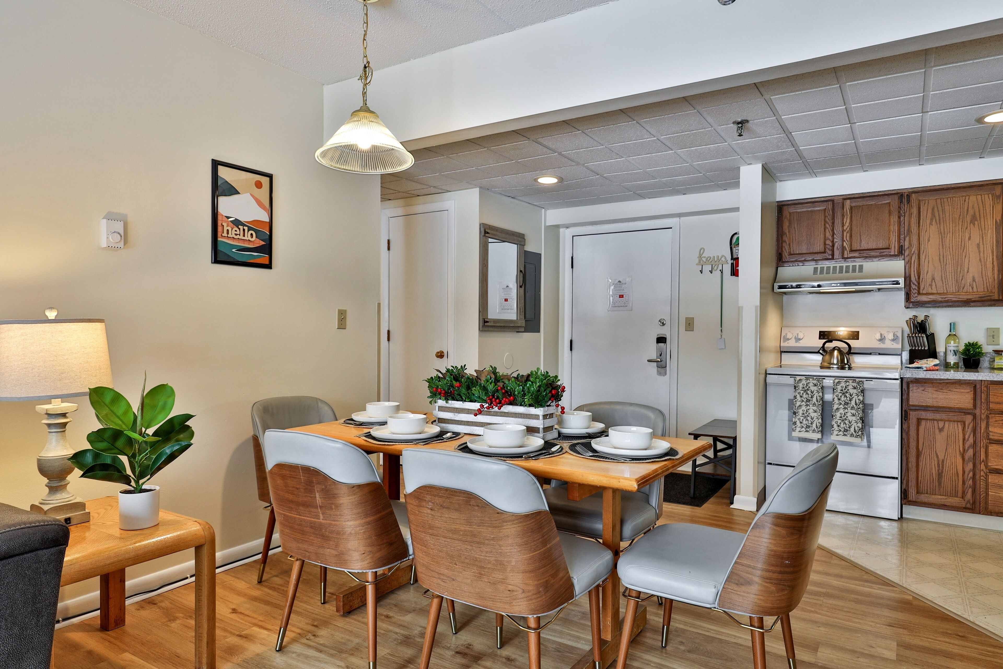 A dining area with a wooden table, grey and brown chairs, a potted plant, and a hanging light fixture.