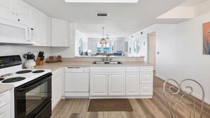 Een moderne keuken met witte kasten, een centraal eiland en uitzicht op de woonkamer.