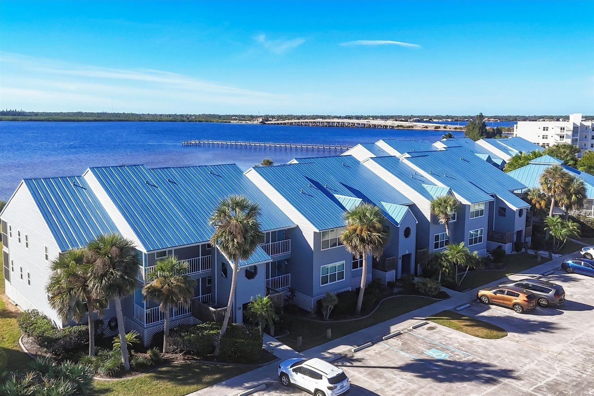 A coastal hotel with blue roofs, a parking lot, and a view of the ocean.