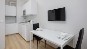 Een moderne keuken met witte kasten, een marmeren aanrecht en een eethoek met een witte tafel en zwarte stoelen.