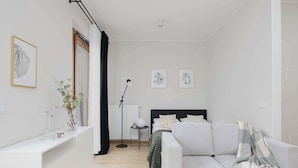 Een moderne, goed verlichte kamer met een witte bank, een bed met een groene deken en een klein nachtkastje met een lamp.