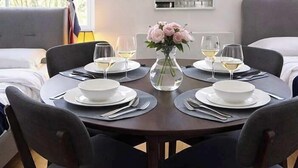 A dining table set for four with white plates, cutlery, and glasses, a vase with flowers, and a window in the background. - Central London (9) Apartment - Hyde Park (Greater London)
