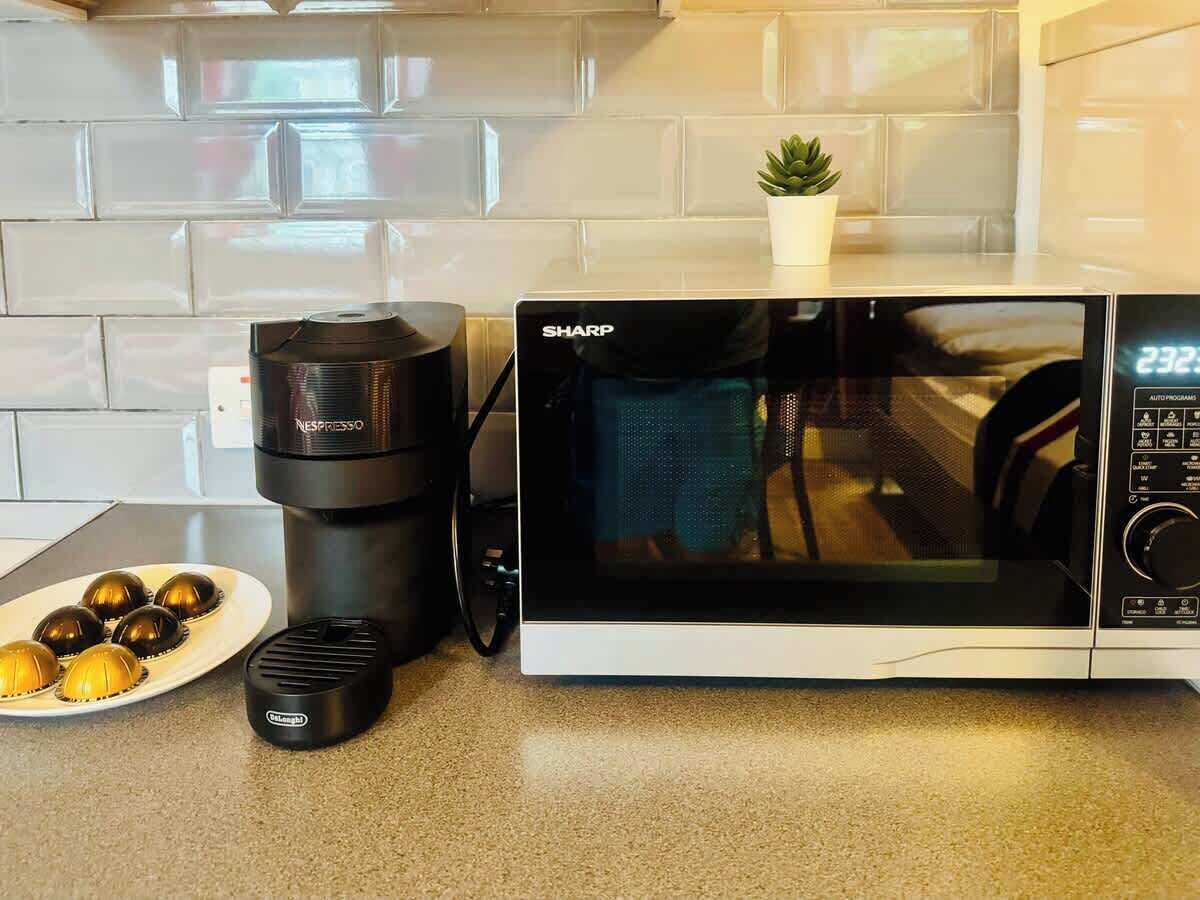 Een keuken met een magnetron, een koffiezetapparaat en een bord met koffiekopjes.