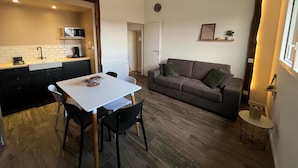 A compact living space with a kitchenette, a dining area, and a seating area with a sofa and a small table. - Apartment 'Les Iris - Cozy House', near Puy du Fou, Clisson and Nantes Vineyards (Montfaucon)