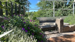A wooden deck with a stone pathway, surrounded by greenery and a metal fence. - Apartment 'Les Iris - Cozy House', near Puy du Fou, Clisson and Nantes Vineyards (Montfaucon)