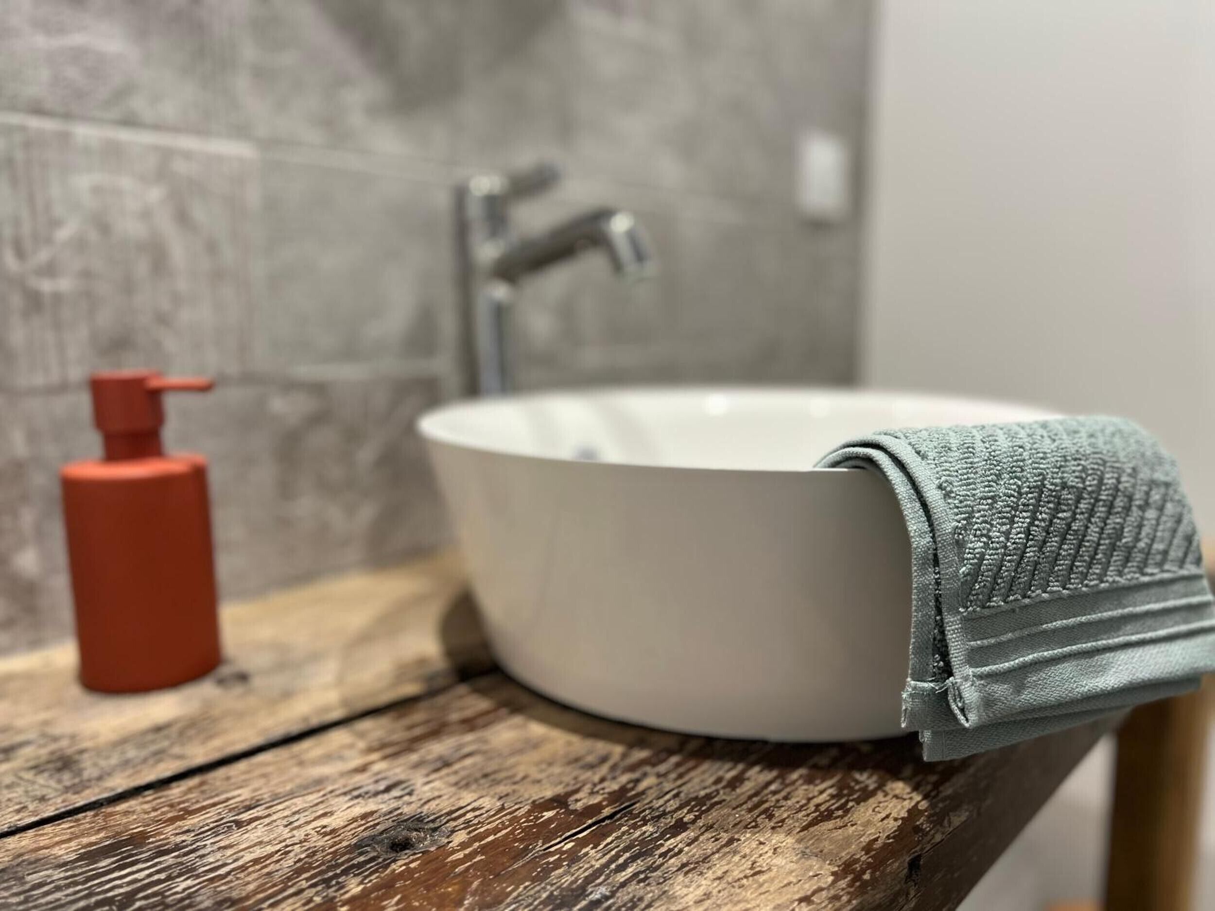 Ein Badezimmer mit einem weißen Waschbecken, einem roten Seifenspender und einer Holzauskład.