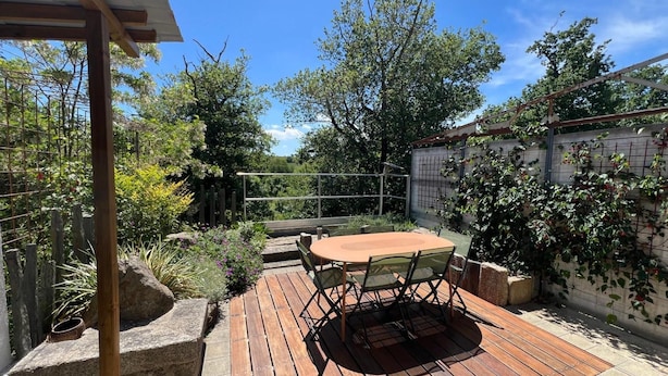 A wooden deck with a round table and chairs, surrounded by greenery and a metal fence. - Apartment 'Les Iris - Cozy House', near Puy du Fou, Clisson and Nantes Vineyards (Montfaucon)