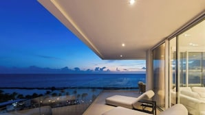 Un balcone moderno con vista sull'oceano, una parete di vetro e un'area salotto con un tavolo.