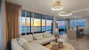 Una sala de estar moderna con un sofá grande, una mesa redonda de centro y vista al océano al atardecer.