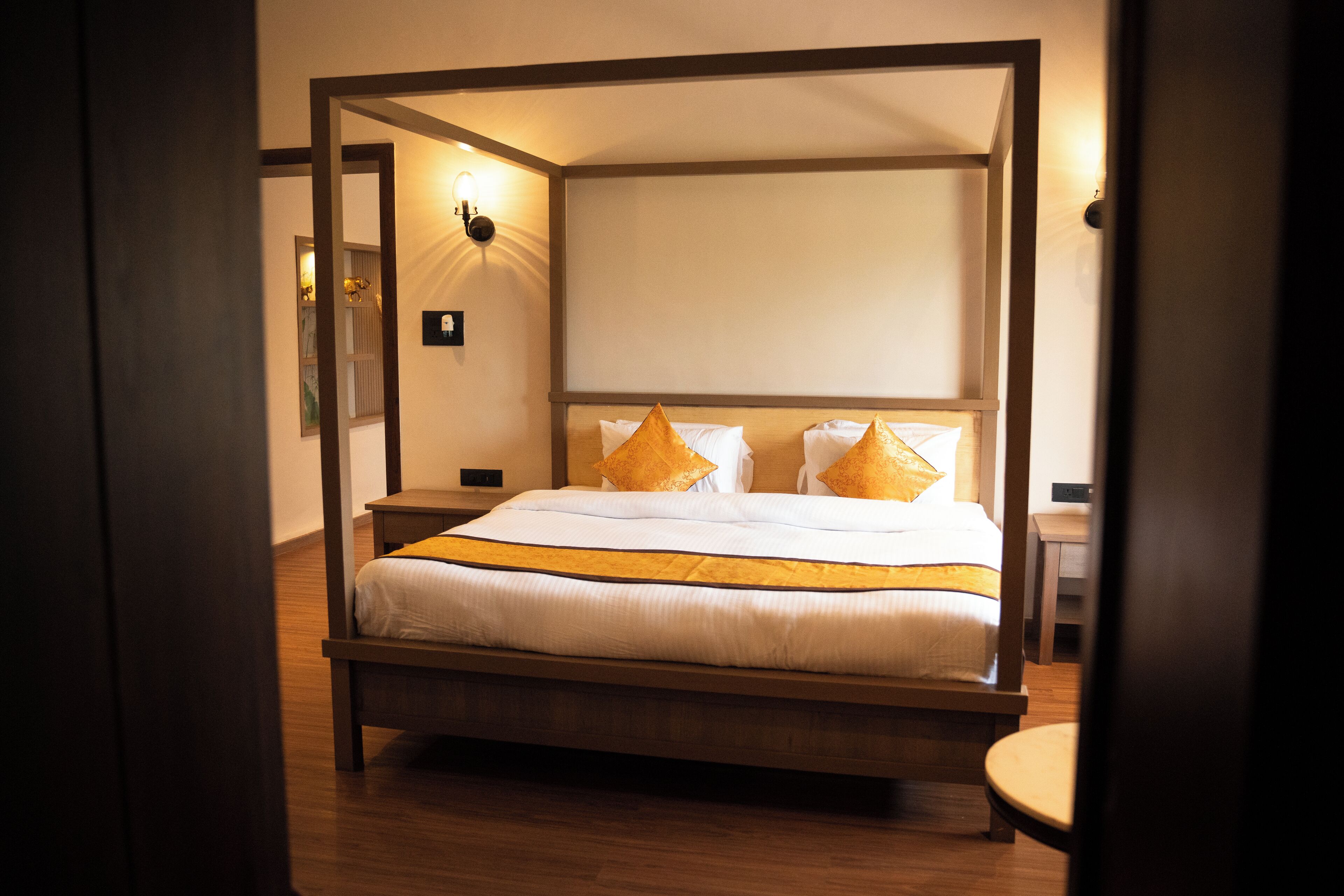 A four-poster bed with a white and gold bedspread, a wooden headboard, and two bedside tables with lamps.