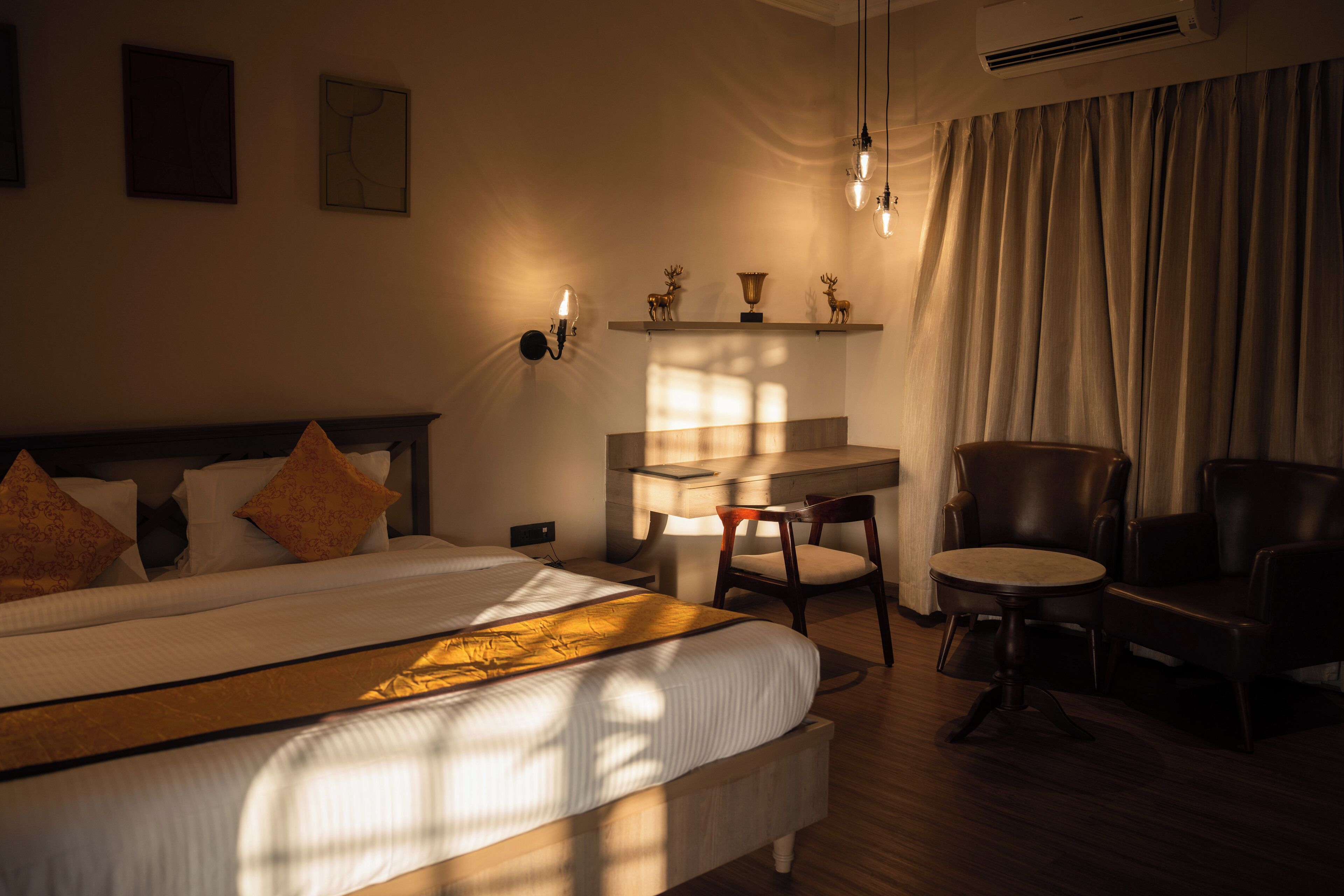 A hotel room with a large bed, a desk, two chairs, and a window with curtains.