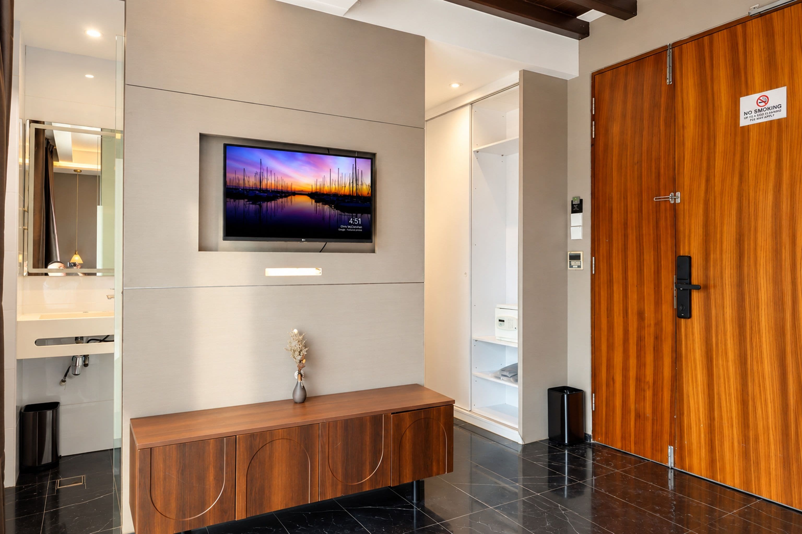 A modern hotel room with a large flat-screen TV mounted on the wall, a wooden console table, and a wooden wardrobe.