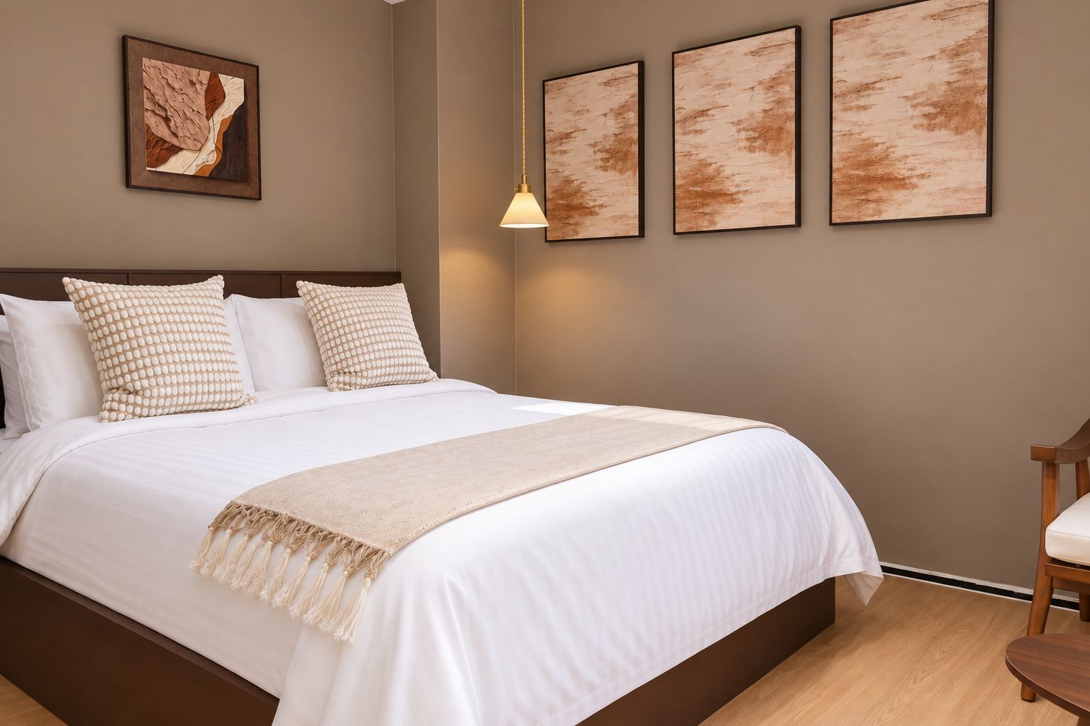 Una cama bien tendida con edredón blanco y manta beige, cabecera de madera y una lámpara colgante.
