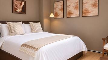 Una cama bien tendida con edredón blanco y manta beige, cabecera de madera y una lámpara colgante.