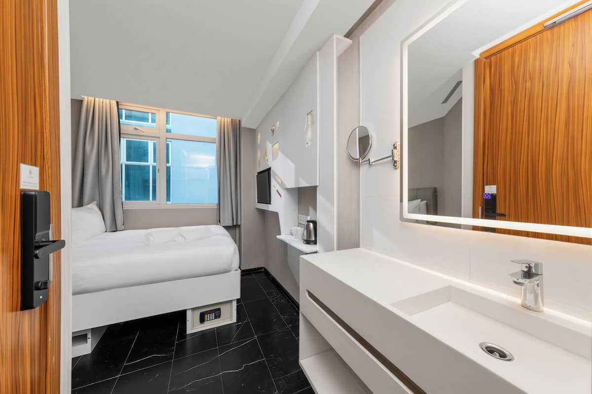 Ein modernes Hotelzimmer mit einem Bett, einem großen Spiegel, einer weißen Kommode und einem Fenster mit Vorhängen.