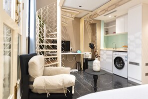 A modern hotel room with a black leather sofa, a white decorative partition, a washing machine, and a small round table with a vase. - Aura Hotel Purvis (Singapore)