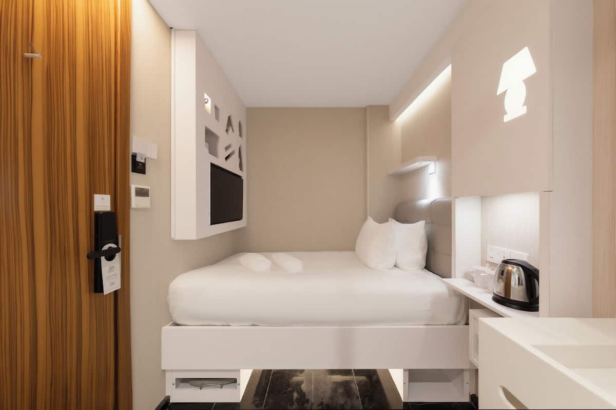 Ein modernes Hotelzimmer mit Bett, Nachttisch und Wandlampe.