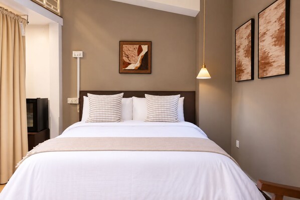 A hotel room with a bed, two pillows, a wall-mounted artwork, a bedside lamp, and a television.
