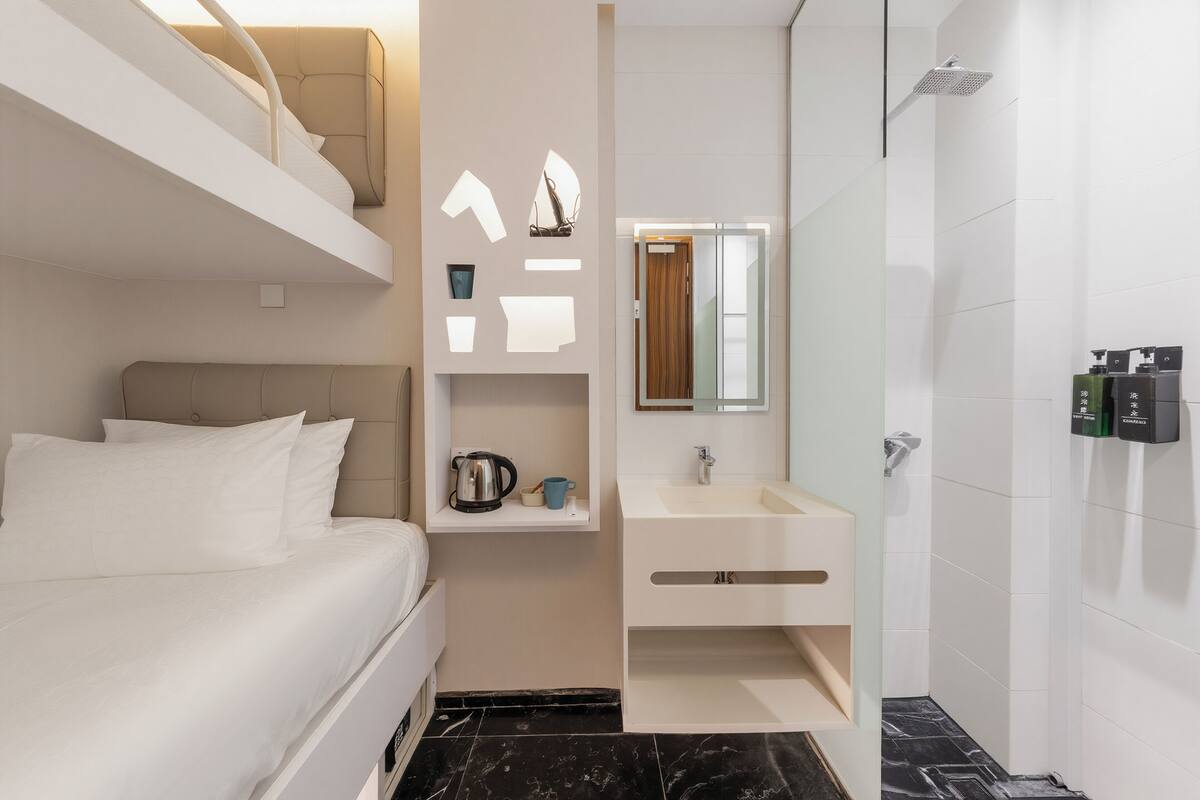 Ein modernes Hotelzimmer mit Bett, einem kleinen Badezimmer mit Waschbecken und Spiegel sowie einer Duschkabine.