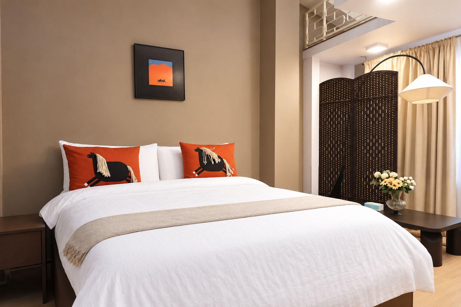 Ein Hotelzimmer mit einem Bett, Kissen, einem Nachttisch, einer Lampe, einer Vase mit Blumen und einem an der Wand hängenden Bild.
