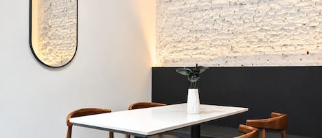 A dining area with a white table, four wooden chairs, a white vase with a plant, and a textured wall.