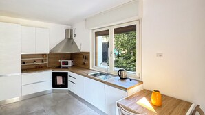A modern kitchen with white cabinets, a wooden countertop, a built-in oven, and a window with a view of greenery. - Casa Mina (Opera)