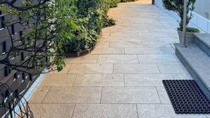 A paved pathway flanked by dense greenery and a modern building with a metal railing. - Casa Mina (Opera)