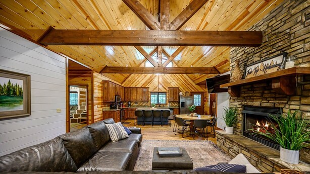 A cozy cabin interior with a stone fireplace, leather sofa, and a dining area. - Treetop Hideaway, Shuffleboard, Hot Tub, Bunks, Games! Free Firewood (Broken Bow)