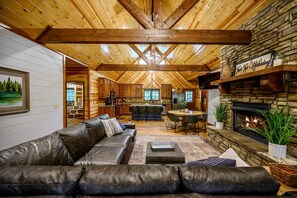Un intérieur de chalet chaleureux avec une cheminée en pierre, un canapé en cuir et un coin repas.