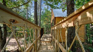 A wooden suspension bridge leading to a rustic cabin in a forest. - Treetop Hideaway, Shuffleboard, Hot Tub, Bunks, Games! Free Firewood (Broken Bow)