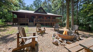 A cabin with a deck, surrounded by trees, featuring outdoor seating and a fire pit. - Treetop Hideaway, Shuffleboard, Hot Tub, Bunks, Games! Free Firewood (Broken Bow)