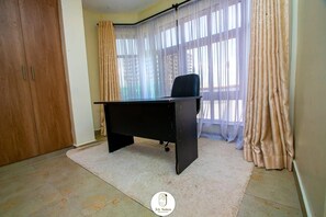 Una habitació amb un escriptori negre, cortines beix i un armari de fusta.