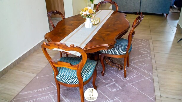 Un coin repas avec une table en bois, quatre chaises et un vase rempli de fleurs.