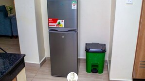 Une cuisine de taille réduite, dotée d’un réfrigérateur en acier inoxydable, d’une poubelle verte et d’un meuble en bois.