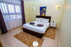 Habitació d'hotel amb un llit, una taula de nit, una làmpada penjada a la paret, un quadre i una finestra amb cortines.