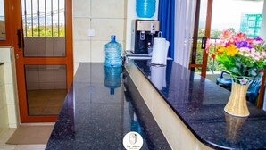 Une chambre d’hôtel dotée d’un comptoir en marbre noir, d’un distributeur d’eau, d’une machine à café et d’un vase rempli de fleurs.