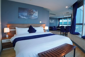 Ein modernes Hotelzimmer mit einem großen Bett, einem Holzkopfschild und Blick auf die Stadt durch große Fenster.