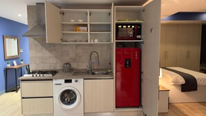 Una cocina compacta con lavadora, un refrigerador rojo y un horno empotrado.